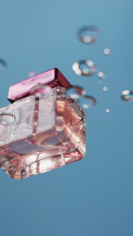 Vertikales-Video-Von-Tropfen,-Die-Auf-Eine-Flasche-Mit-Schönheitsprodukt-Fallen,-Mit-Kopierraum-Auf-Blauem-Hintergrund