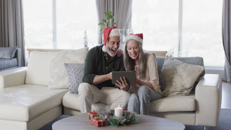 Middle-aged-caucasian-couple-in-santa-hats-on-tablet-video-chat-at-christmas-at-home,-slow-motion