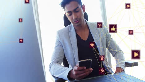 Animation-of-connected-icons-globes-over-biracial-man-sitting-on-chair-and-using-cellphone-at-office