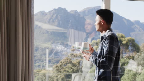 Hombre-Afroamericano-Tomando-Café-En-La-Ventana-Con-Vistas-Soleadas-A-La-Montaña,-Espacio-Para-Copiar,-Cámara-Lenta