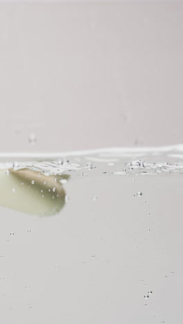 Vídeo-Vertical-Del-Tubo-De-Un-Producto-De-Belleza-Cayendo-Al-Agua-Con-Espacio-Para-Copiar-Sobre-Fondo-Azul