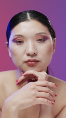 Vertical-video-of-asian-woman-with-black-hair-and-make-up-looking-at-camera,-copy-space,-slow-motion
