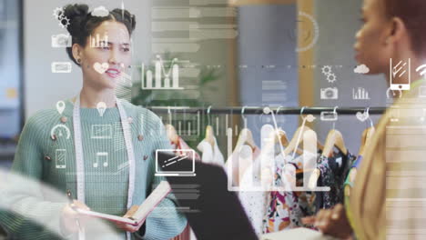 Animation-of-computer-icons-and-coding-over-diverse-female-colleagues-discussing-in-clothing-studio