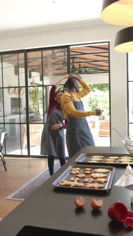 Vertical-video-of-happy-diverse-couple-baking-christmas-cookies-dancing-in-kitchen,-slow-motion