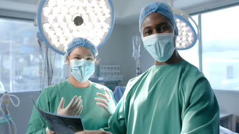 Portrait-of-diverse-female-and-male-surgeon-in-masks-with-x-ray-in-theatre,-slow-motion