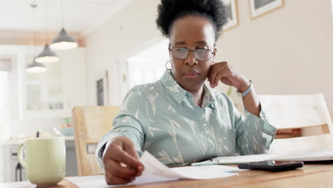 Happy-african-american-senior-woman-doing-paperwork-and-using-laptop-in-sunny-room,-slow-motion