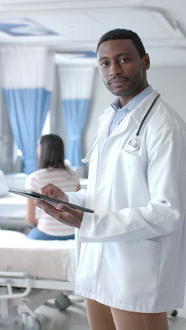 Vertical-video-portrait-of-smiling-african-american-male-doctor-using-tablet,-slow-motion