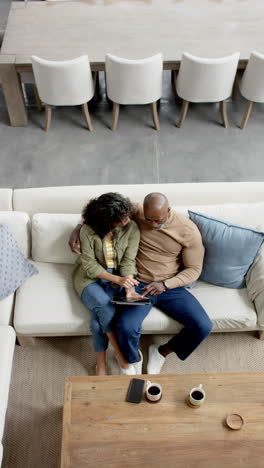 Video-Vertical-De-Una-Feliz-Y-Diversa-Pareja-Madura-En-El-Sofá-Usando-Tableta,-Espacio-Para-Copiar,-Cámara-Lenta