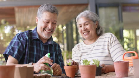 Feliz-Y-Diversa-Pareja-De-Ancianos-Sentada-A-La-Mesa-Y-Plantando-Plantas-En-Macetas-En-El-Porche