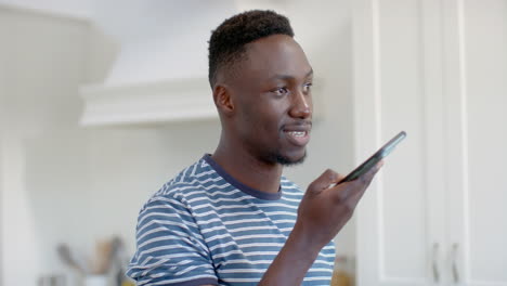 Happy-african-american-man-using-smartphone-and-smiling-in-sunny-kitchen,-slow-motion