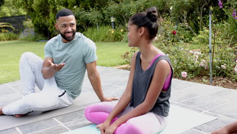 Feliz-Padre-Afroamericano,-Hija-E-Hijo-Haciendo-Yoga-Sentados-En-El-Jardín-Hablando,-Cámara-Lenta