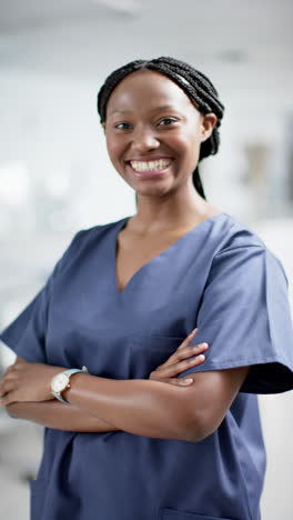 Vertical-video-of-portrait-of-happy-african-american-female-doctor-in-hospital,-slow-motion