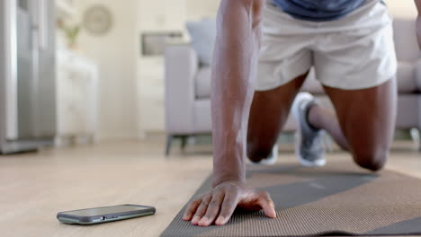 African-american-man-doing-mountain-climbers-using-smartphone-in-living-room,-slow-motion