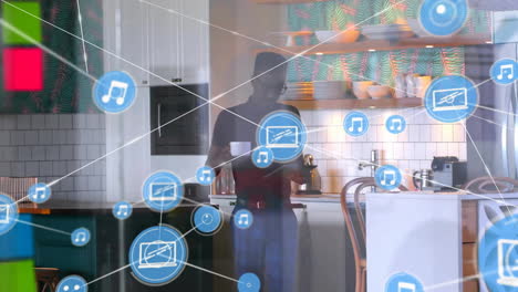 Animation-of-network-of-connections-with-icons-over-biracial-man-in-kitchen