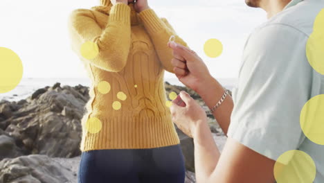 Animation-of-light-spots-over-african-american-couple-proposing-on-beach