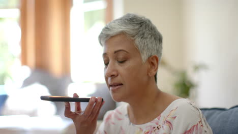 Happy-senior-biracial-woman-sitting-on-couch-and-talking-on-smartphone-at-home,-slow-motion