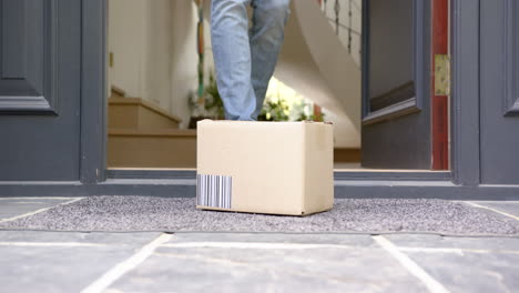 Low-section-of-biracial-man-picking-up-delivery-in-cardboard-box-outside-front-door,-slow-motion