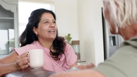 Fröhliche,-Vielfältige-Seniorinnen-Diskutieren-Und-Lächeln-Auf-Dem-Sofa-Im-Sonnigen-Wohnzimmer,-Zeitlupe