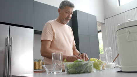 Feliz-Hombre-Birracial-Mayor-Preparando-Ingredientes-Para-Un-Batido-Saludable-En-La-Cocina-De-Casa,-Cámara-Lenta