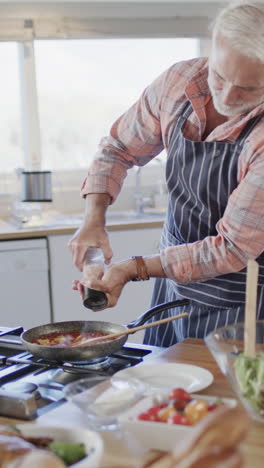 Vertical-video-of-senior-caucasian-man-preparing-dinner-in-kitchen,-slow-motion