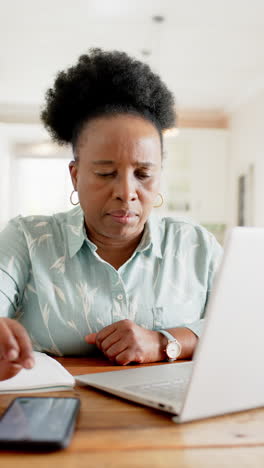 Afroamerikanische-Seniorin-Erledigt-Papierkram,-Benutzt-Laptop,-Smartphone-Im-Sonnigen-Zimmer,-Zeitlupe