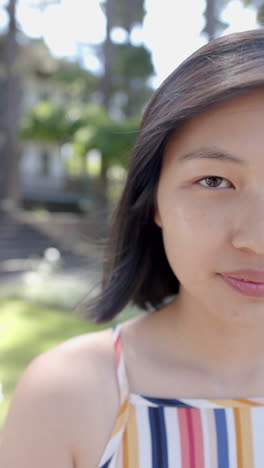 Halbes-Gesicht-Einer-Glücklichen-Asiatischen-Frau-Mit-Dunklem-Haar,-Die-Im-Sonnigen-Garten-Steht-Und-Lächelt,-Zeitlupe