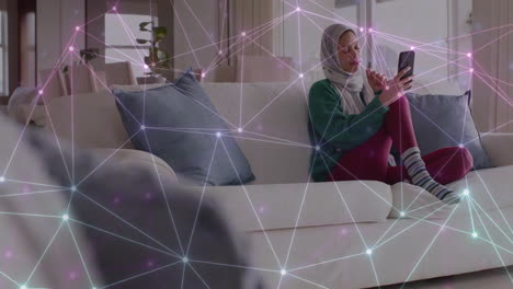 Animation-of-network-of-connections-over-biracial-woman-in-hijab-using-tablet