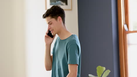 Focused-biracial-man-talking-on-smartphone-in-pacing-sunny-living-room,-slow-motion