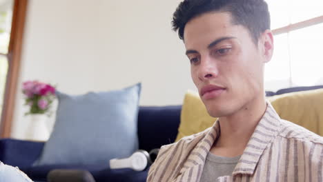 Focused-biracial-man-sitting-on-floor-using-smartphone-in-living-room,-slow-motion