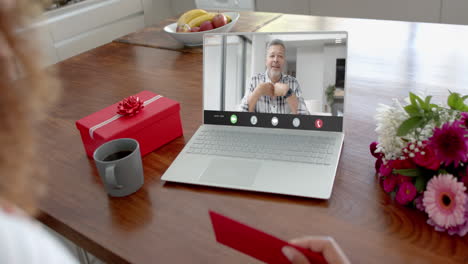 Caucasian-woman-holding-red-envelope-using-laptop-with-caucasian-man-on-screen