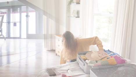 Animation-of-happy-caucasian-woman-packing-suitcase-in-bedroom-over-travellers-wheeling-suitcases