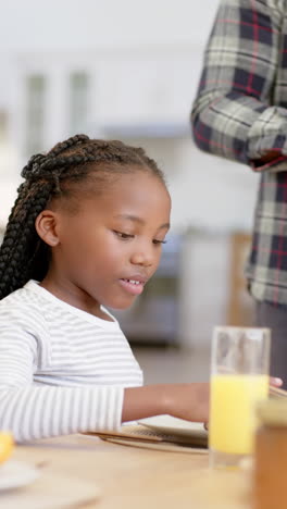 Video-Vertical-De-Una-Feliz-Niña-Afroamericana-Con-Su-Padre-Desayunando-En-Casa,-Cámara-Lenta