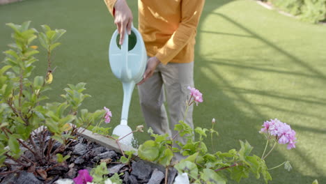 Glücklicher-Biracial-Mann,-Der-Pflanzen-Im-Sonnigen-Garten-Gießt,-Kopierraum,-Zeitlupe