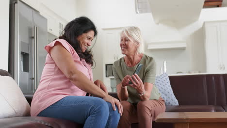 Mujeres-Mayores-Felices-Y-Diversas-Usando-Teléfonos-Inteligentes-Y-Discutiendo-En-Una-Sala-De-Estar-Soleada,-En-Cámara-Lenta