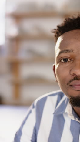 Half-face-of-african-american-man-with-beard-sitting-and-smiling-in-pottery-studio,-slow-motion