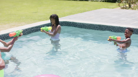 Felices-Padres-Afroamericanos-E-Hija-Jugando-Con-Pistolas-De-Agua-En-Una-Piscina-Soleada,-Cámara-Lenta