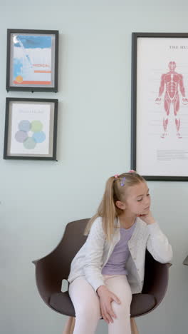 Vertical-video-caucasian-girl-patient-sitting-waiting-in-hospital-reception,-copy-space,-slow-motion