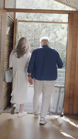 Vertical-video-of-happy-senior-caucasian-couple-walking-through-door-with-suitcase,-slow-motion