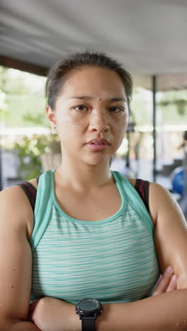 Serious-asian-woman-standing-with-folded-arms-in-sunny-home-gym,-slow-motion