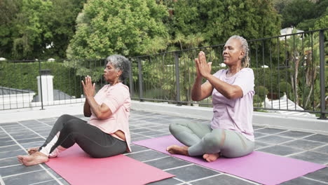 Amigas-Afroamericanas-Mayores-Practicando-Meditación-De-Yoga-Sentadas-En-El-Balcón,-Cámara-Lenta