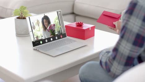 Caucasian-man-holding-envelope-and-talking-with-african-american-woman-on-laptop-screen