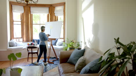 Mujer-Birracial-Mayor-Usando-Delantal-Y-Pintando-Sobre-Lienzo-Grande-En-Casa,-Cámara-Lenta