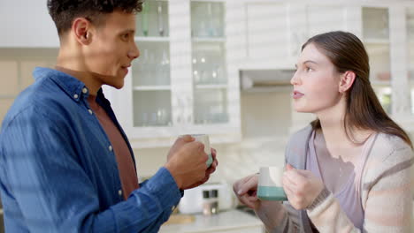 Happy-diverse-couple-talking-and-drinking-coffee-in-kitchen-at-home,-in-slow-motion