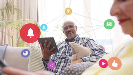 Animation-of-network-of-connections-with-icons-over-senior-african-american-man-using-tablet