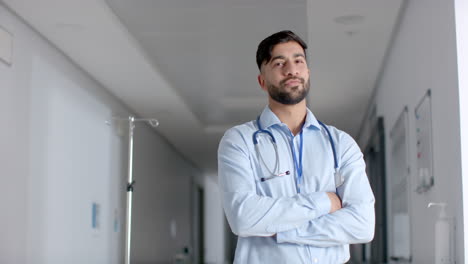 Portrait-of-biracial-male-doctor-wearing-lab-coat-in-hospital-corridor,-copy-space,-slow-motion