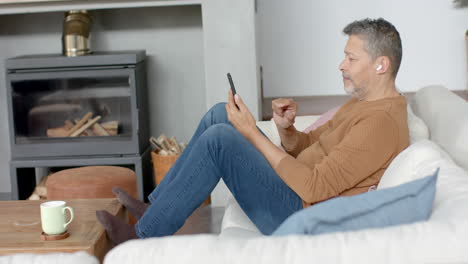 Senior-biracial-man-using-smartphone-and-earphones-sitting-on-couch-in-living-room,-slow-motion