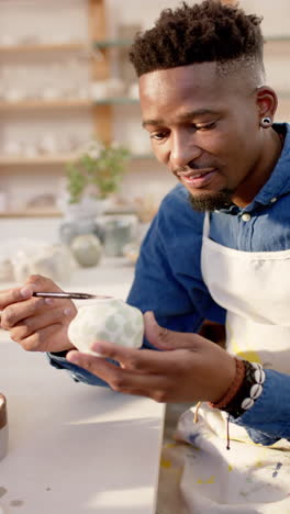 Happy-african-american-potter-glazing-clay-jug-and-smiling-in-pottery-studio,-slow-motion