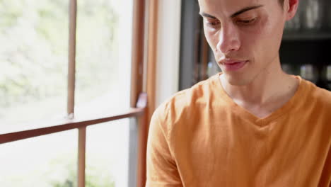 Thoughtful-biracial-man-using-tablet-by-window-in-living-room,-copy-space,-slow-motion