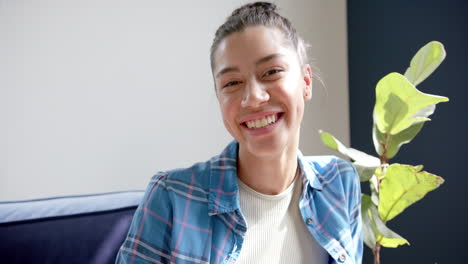 Portrait-of-happy-biracial-teenage-girl-sitting-in-sunny-room-at-home-smiling,-slow-motion