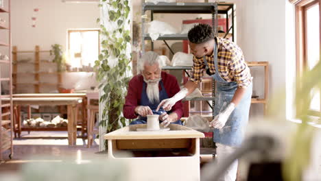 Focused-diverse-male-potters-using-potter's-wheel-in-pottery-studio,-slow-motion